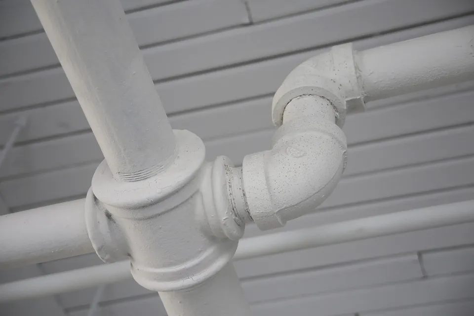 White painted pipes and fittings running along a ceiling