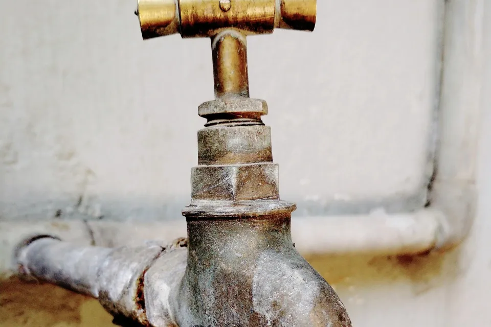 Old corroded brass faucet on a pipe against a wall